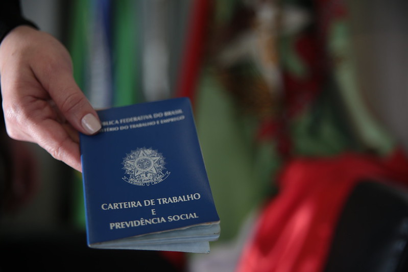 Foto mostra carteira de trabalho com a bandeira de Santa Catarina ao fundo