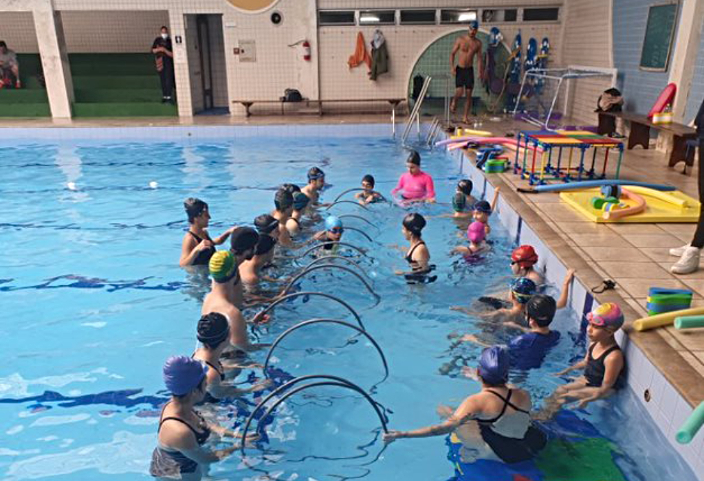 Diversas crianças praticam natação em piscina coberta