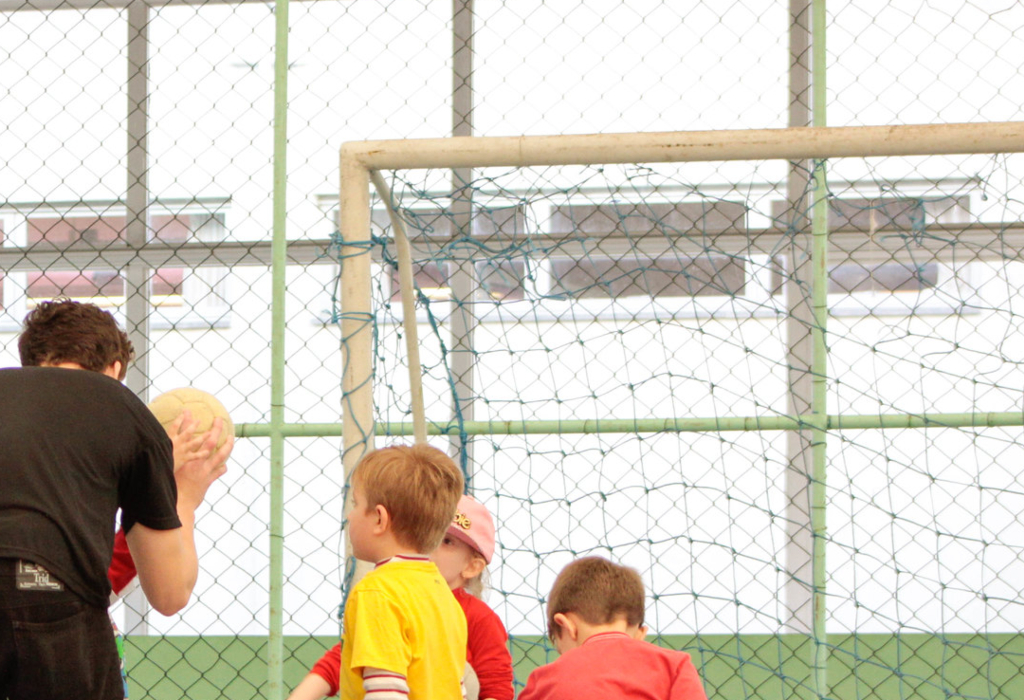 Crianças escutam explicação de acadêmico de Educação Física sobre jogo com bola