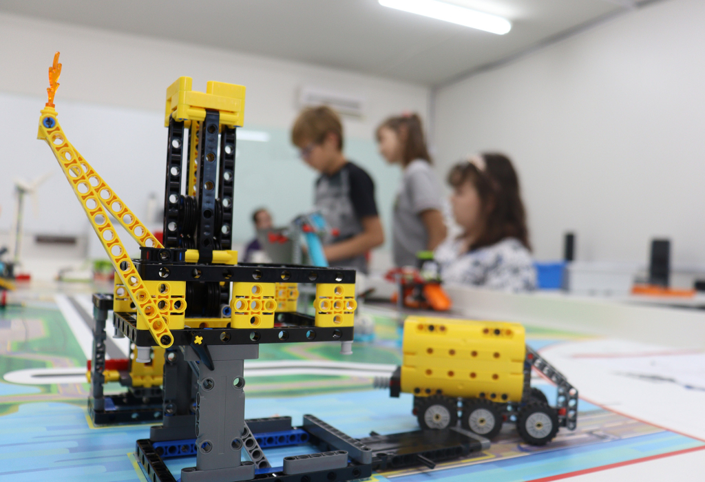 Em primeiro plano, aparecem robôs montados com peças de Lego. Ao fundo, alunos do curso de extensão da universidade.