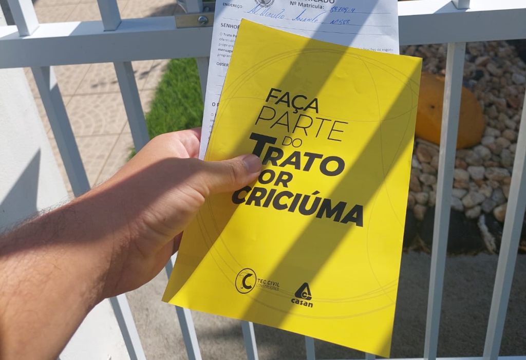 Profissional do Trato por Criciúma entrega panfleto e comunicado no portão de uma casa.