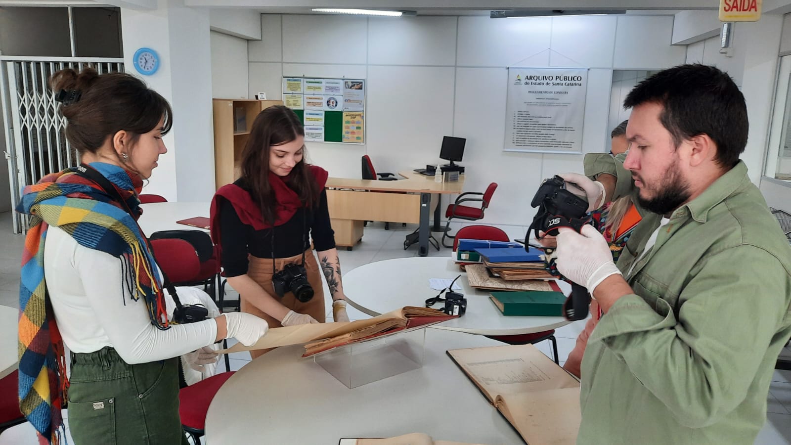 Dois estudantes da Udesc manipulam documentos históricos enquanto um fotografa