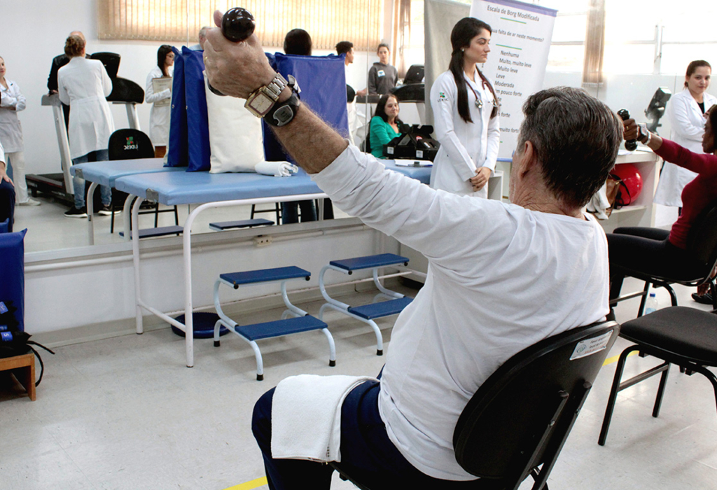 Paciente de meia-idade em reabilitação faz exercício sentado erguendo pequeno halter
