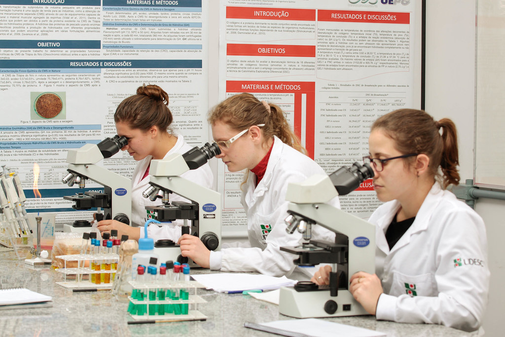 Três estudantes olham microscópios em laboratório da Udesc