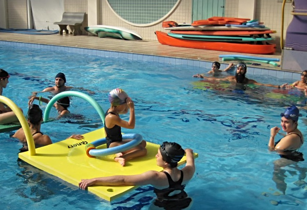 Crianças aprendem natação sob orientação de monitores da universidade.