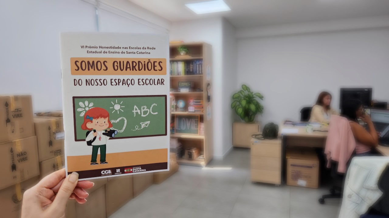 Mão segura cartilha do Prêmio Honestidade nas Escolas