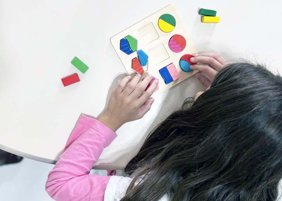 Menina mexe em peças coloridas sobre mesa branca.